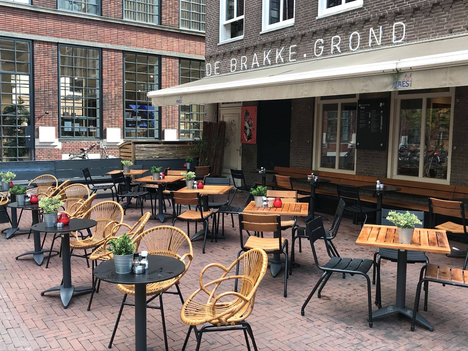 Het terras met rotan stoelen onder de luifel van De Brakke Grond